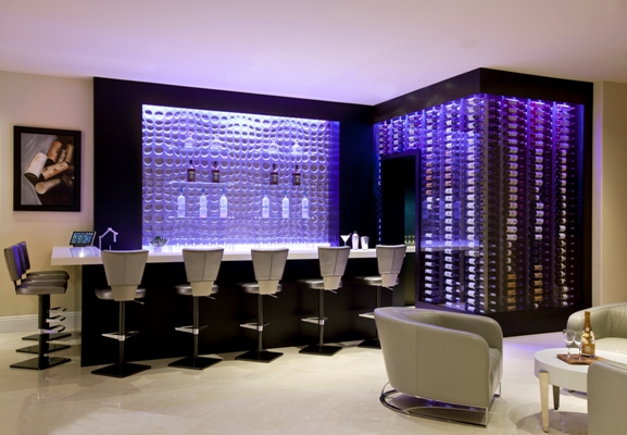 Adega da Wine Cellar Designs chamativa e luxuosa em sala de estar estilo bar com poltronas e cadeiras  brancas